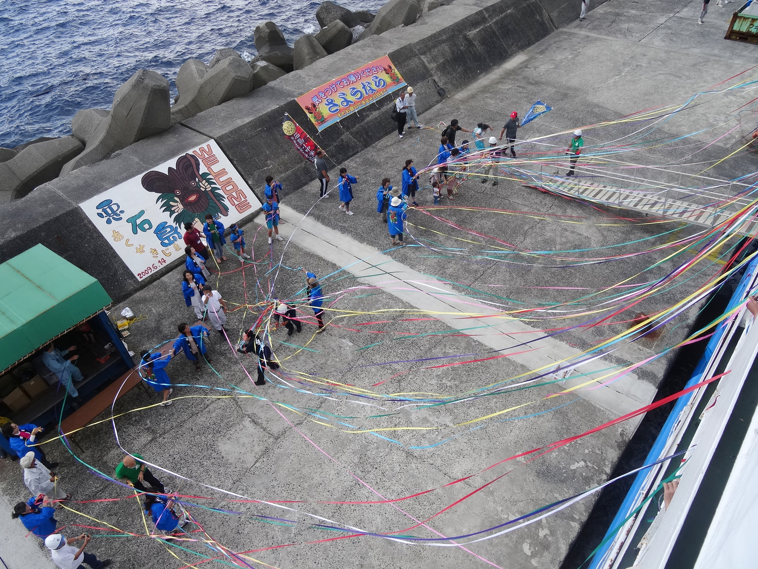 悪石島のフェリー出航風景。防波堤上の人々と色とりどりの紙テープ