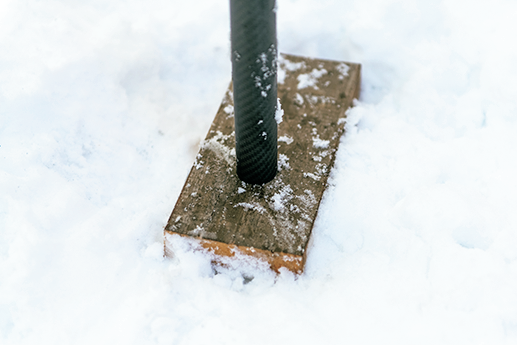 雪の上に木片を置き、その上にテントポールを立てる