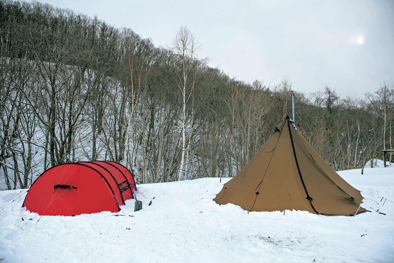 雪の上に立つオレンジ色のかまぼこ型テントと茶色のピラミッド型テント