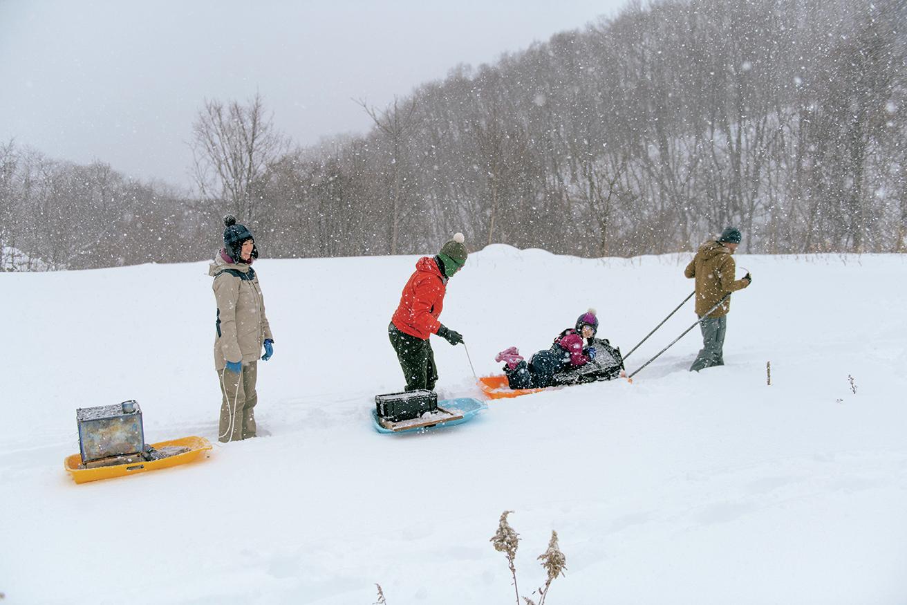 雪の中でそりに乗った子供とそりを引く3人の大人