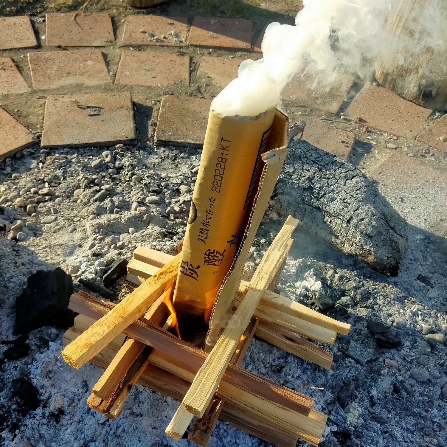 井桁に組んだ薪の中央に円筒形の段ボールを刺した状態。下部から炎が、上部から煙が出ている
