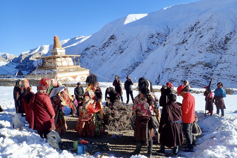 ヒマラヤ奥地の冬の祭り。雪の山と仏塔と祈る人々