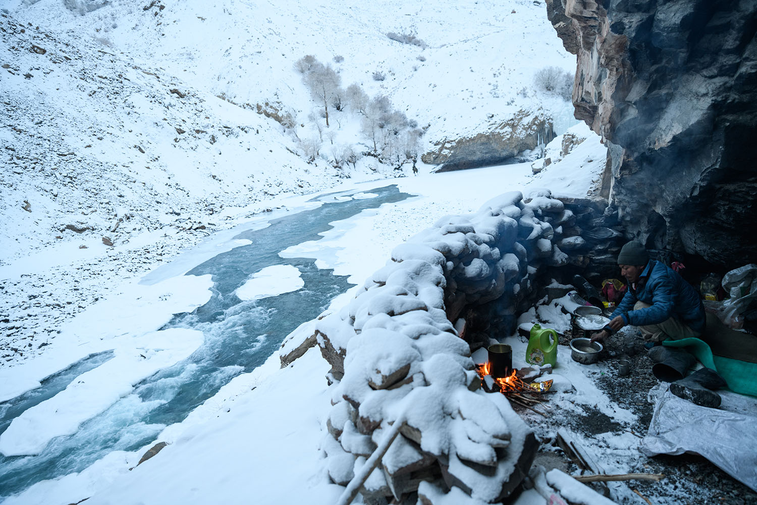 ヒマラヤ奥地の雪の覆われた小川のほとりで焚き火をしながら朝食