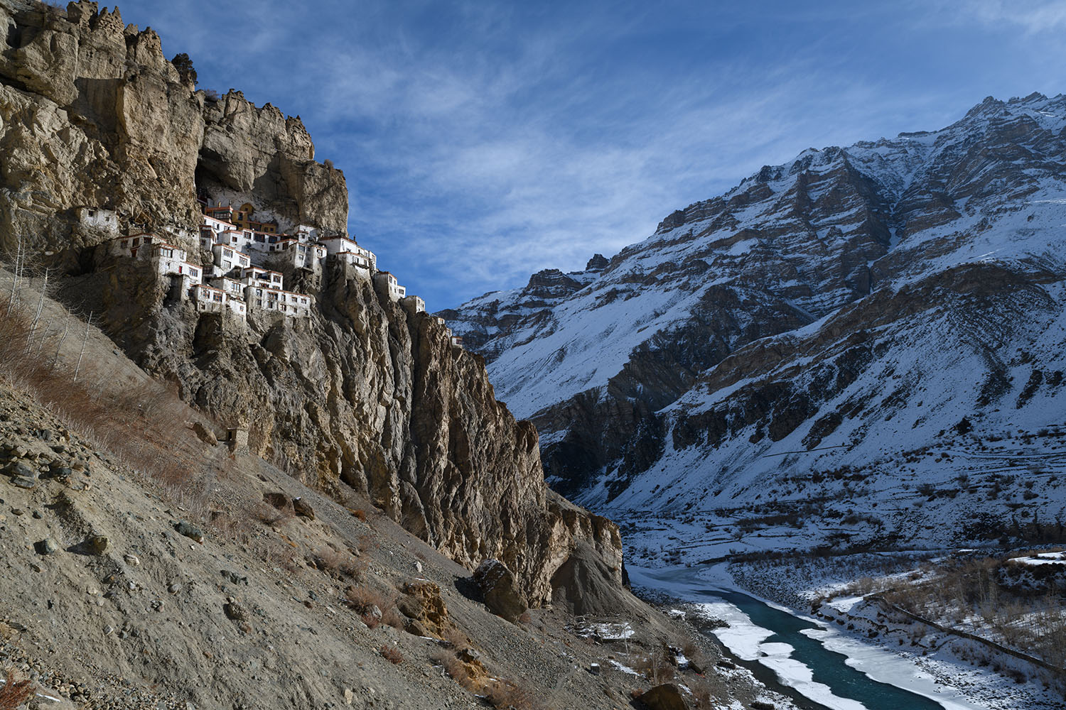 プクタル・ゴンパの全景。雪景色の山と川。断崖絶壁に家々が張り付いている