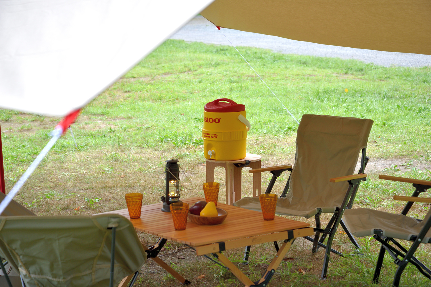 キャンプのタープの下にテーブル、チェア、ウォータージャグ