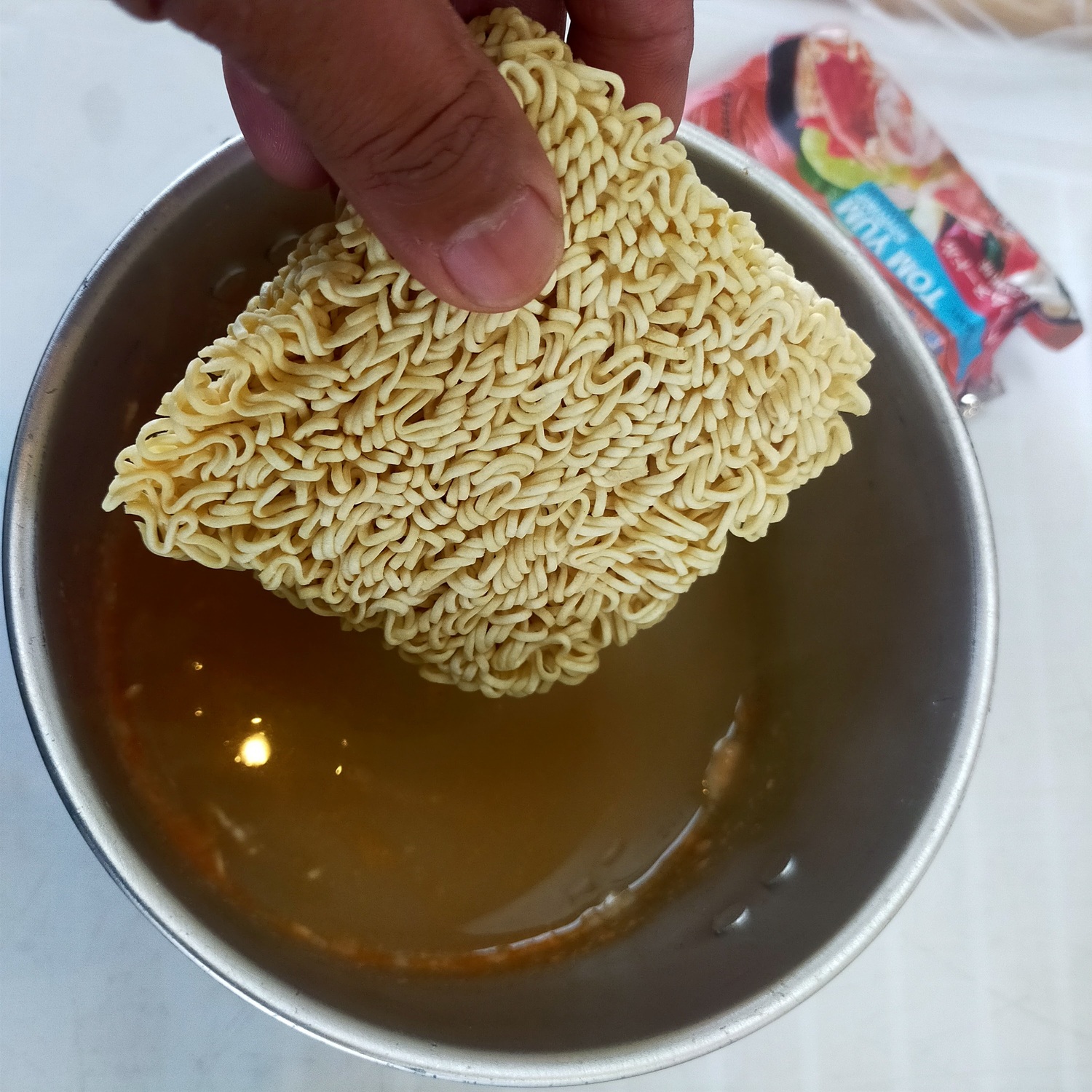 殻を取り除いただし汁入りのお湯にラーメンを入れている