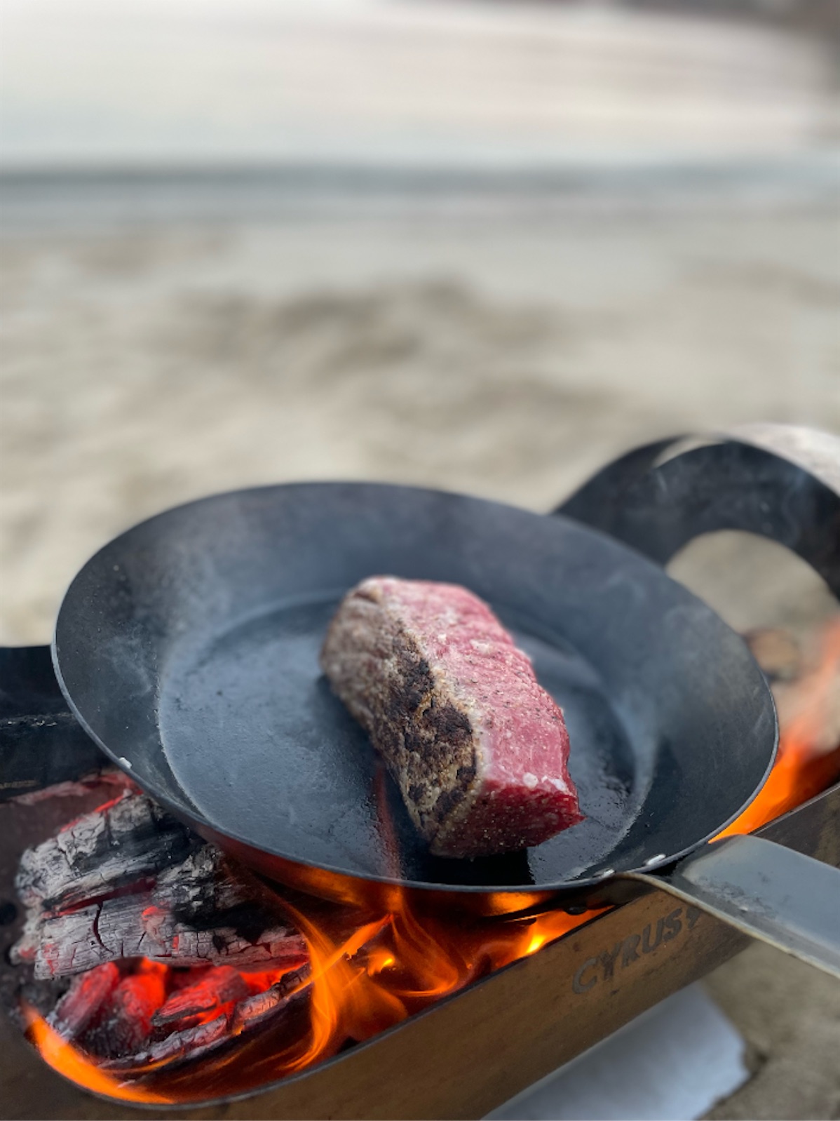 焚き火台にフライパンをのせてステーキを焼いている