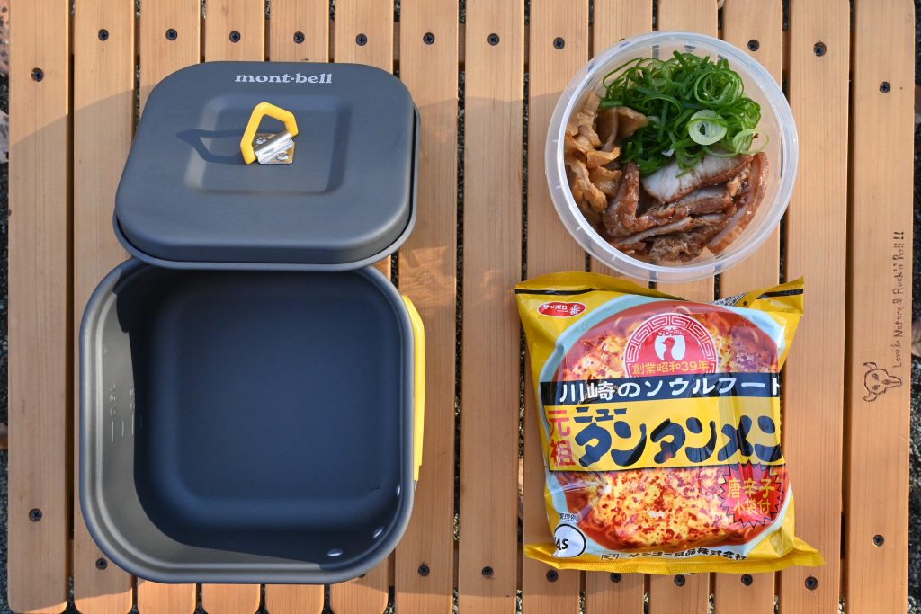 机に角形クッカー、袋ラーメン、具材が並んでいる様子。