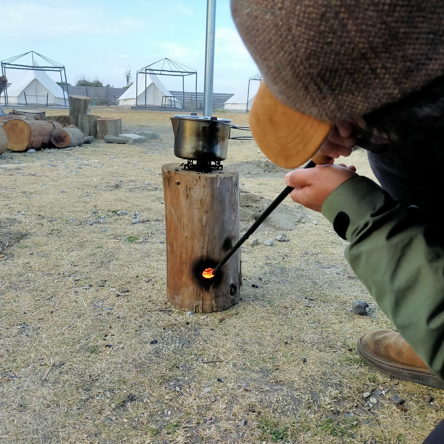 丸太ストーブの側面の穴に、火吹き棒で空気を送っている。