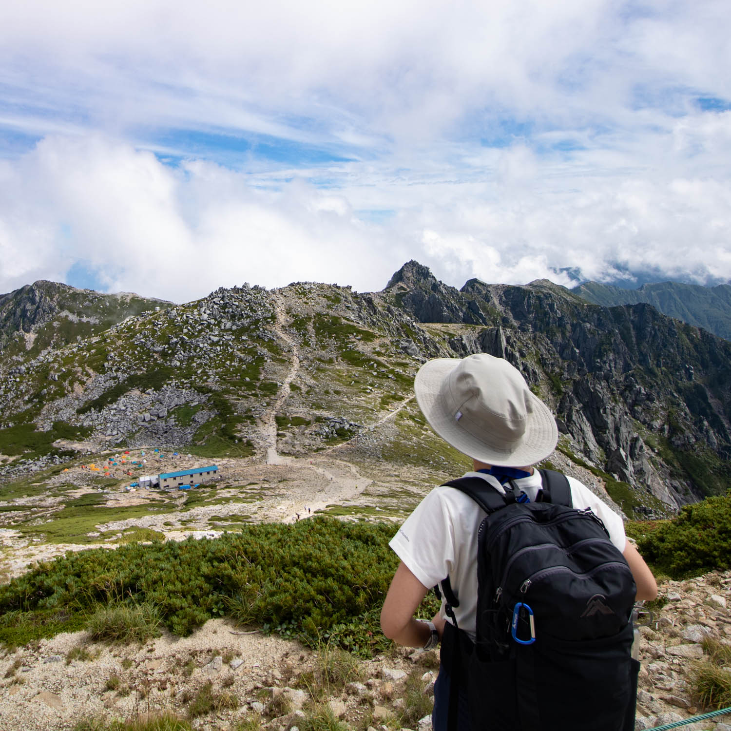 帽子をかぶった女性が山の稜線を眺めている。