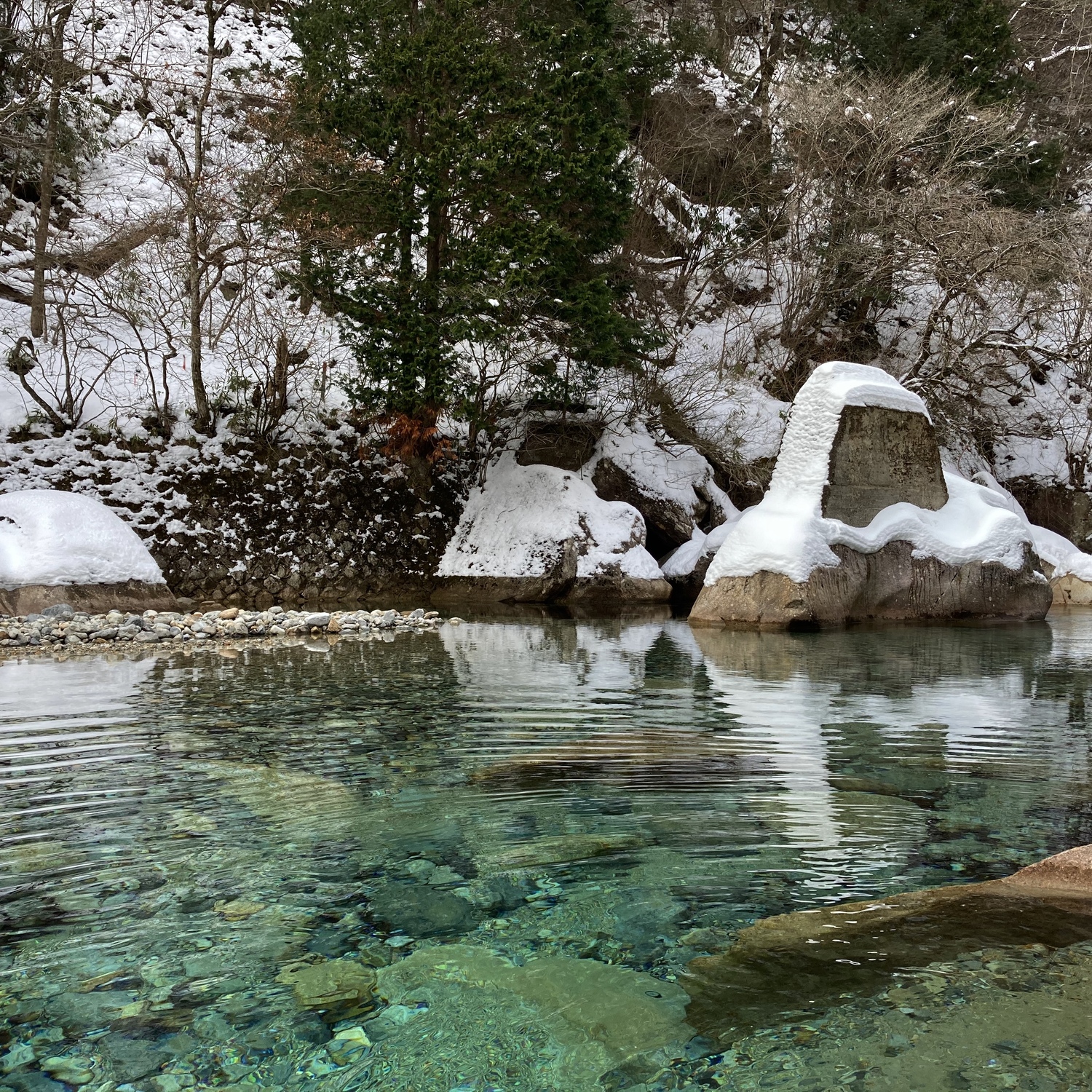 雪が積もった岩の前に湖が流れている。