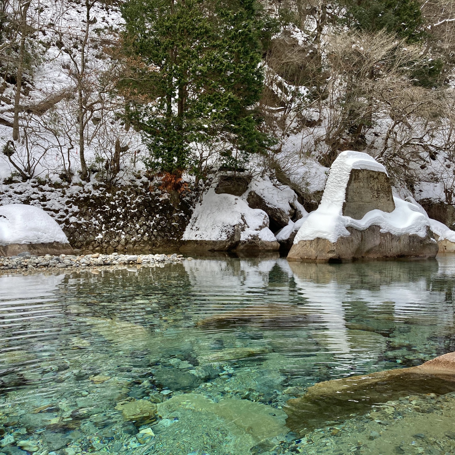 雪の積もった岩の前に湖が流れている。