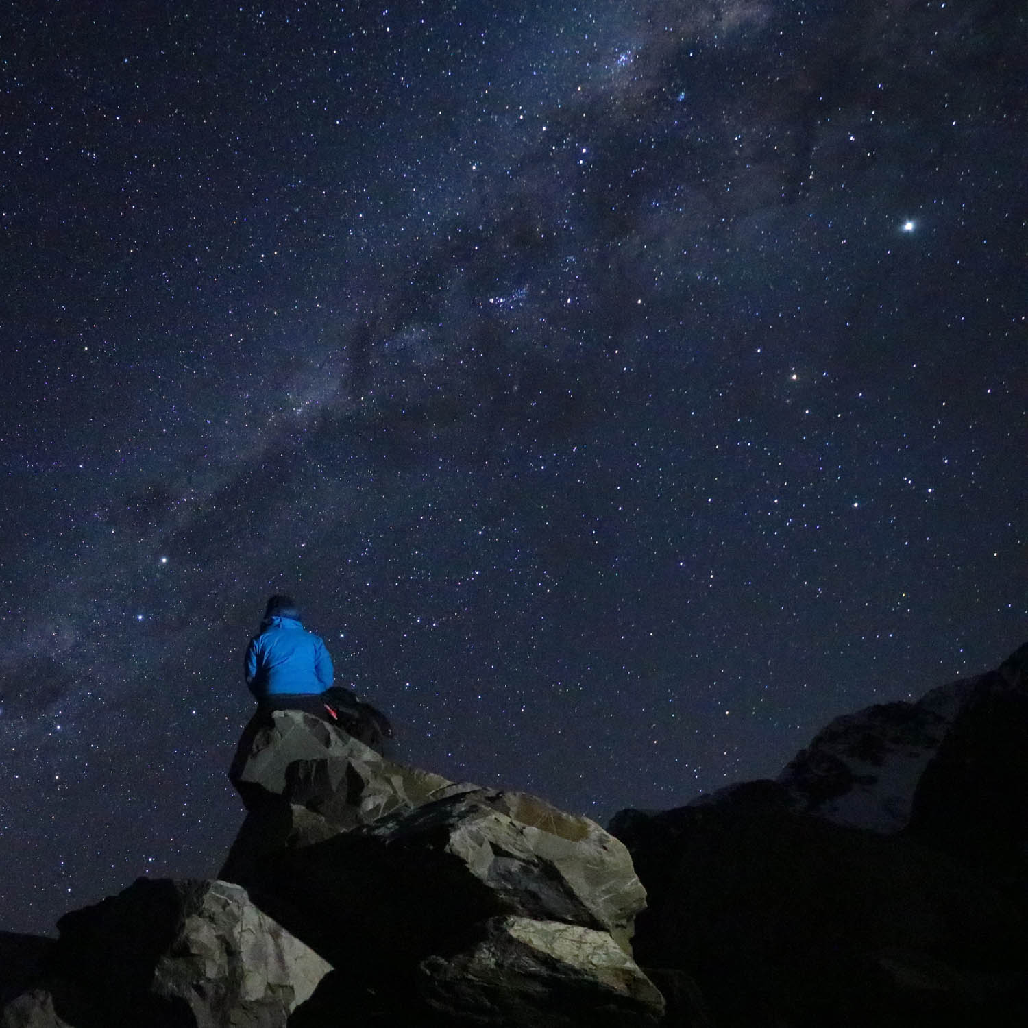 女性が山の上で星空を眺めている。