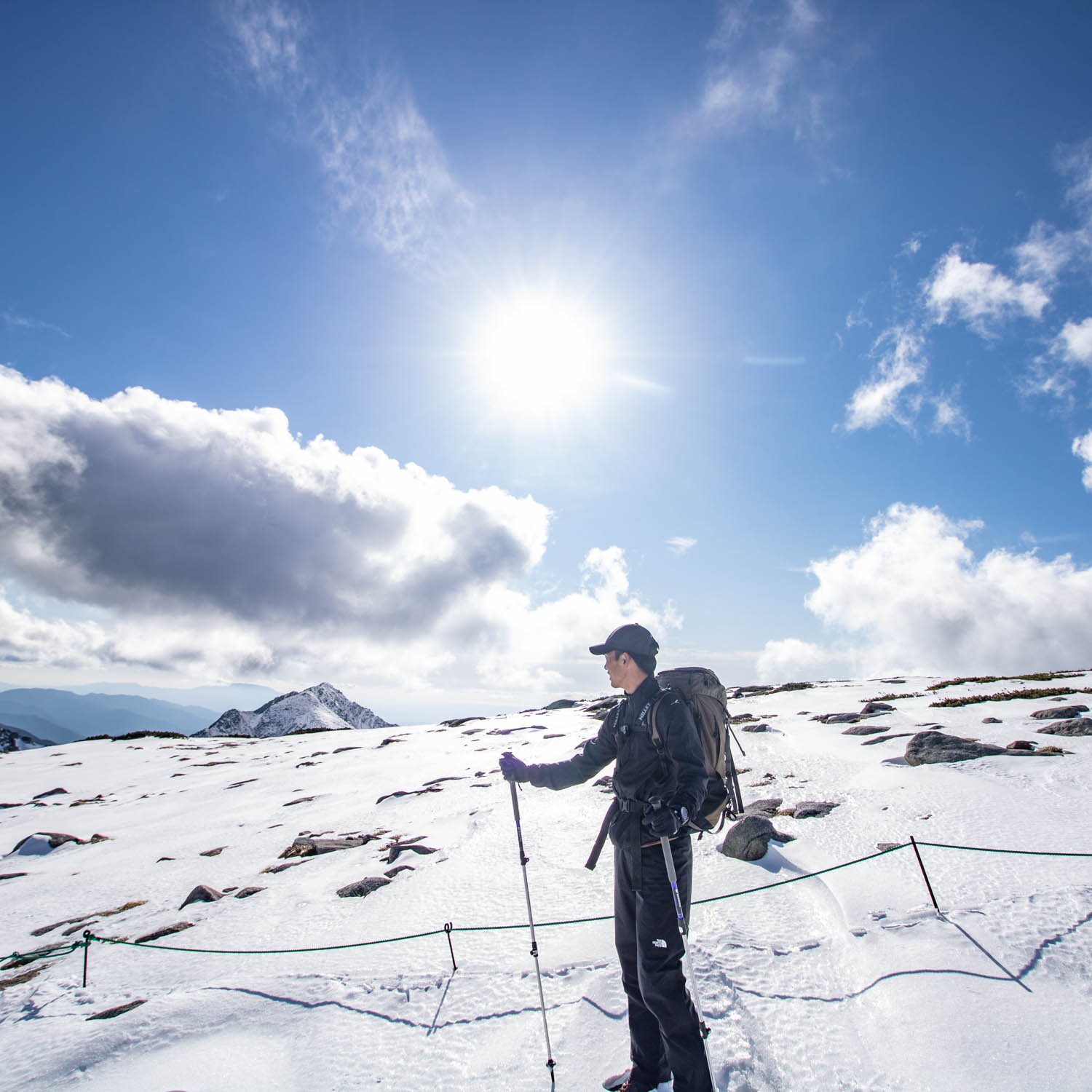 レインウェアを着た登山者が雪山に立っている。