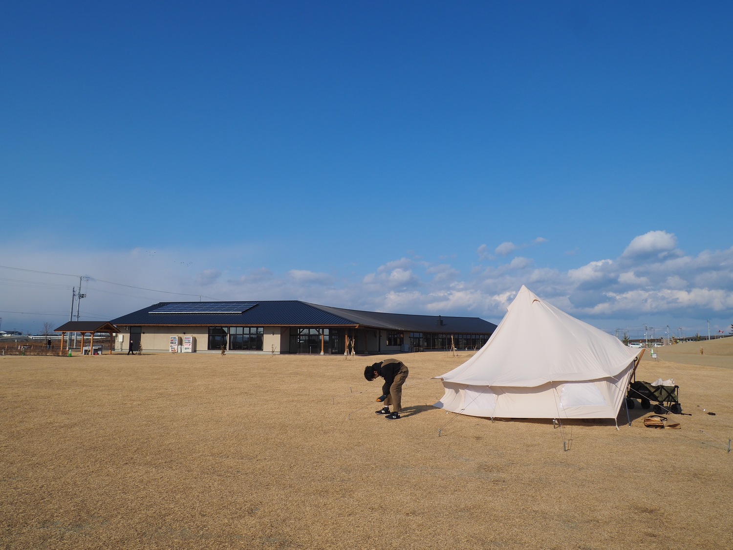 青空のキャンプ場で白いテントを張る青年