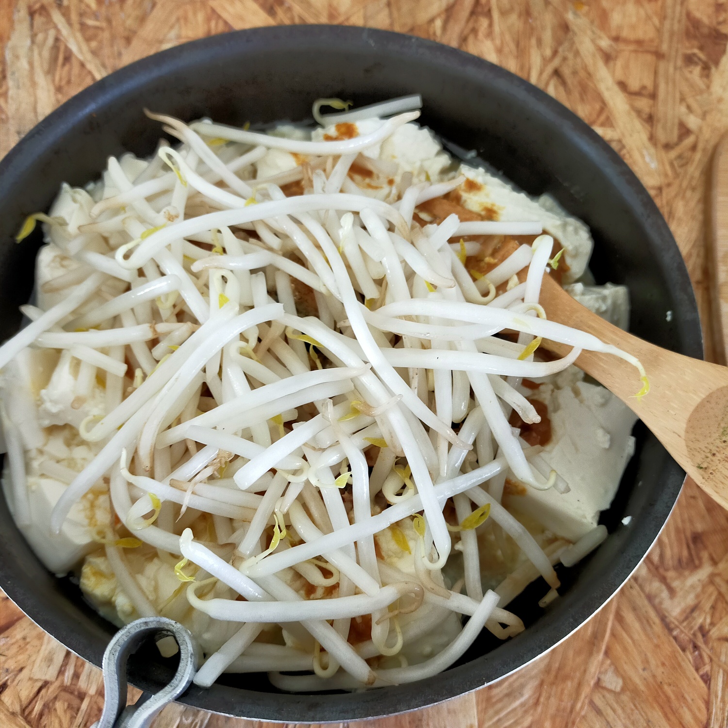 フライパンの中に豆腐があり、その上にもやしが盛られている。
