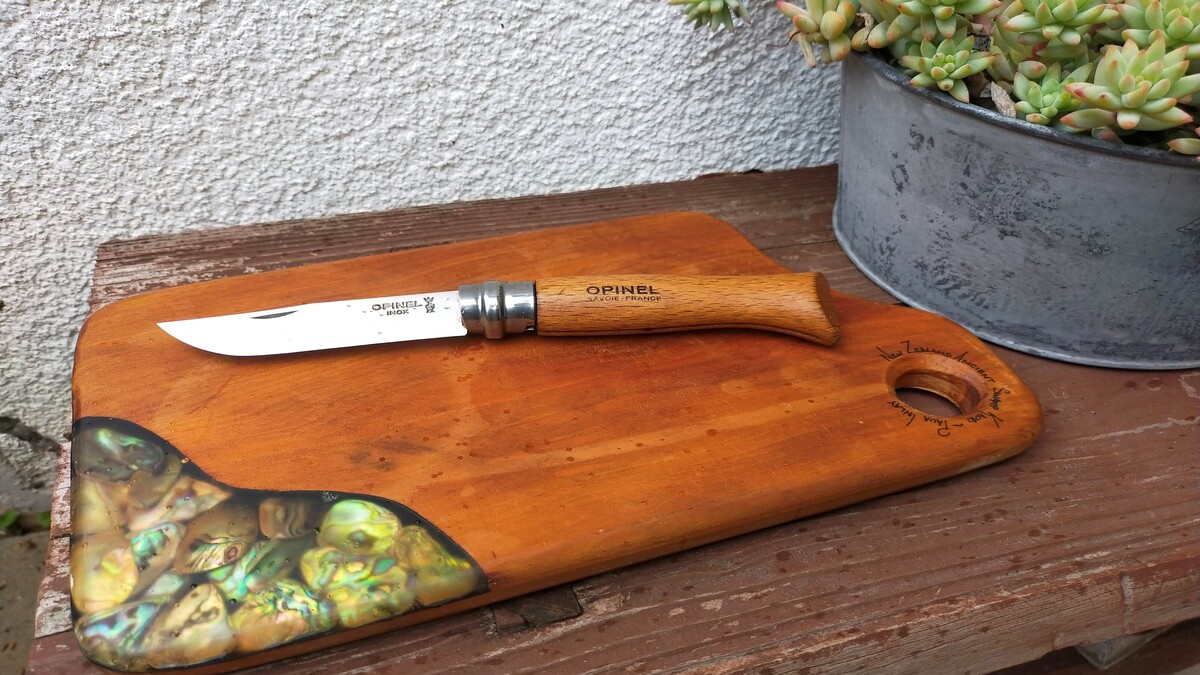 屋外の棚の上に木のまな板と、木の柄のナイフが載っている。