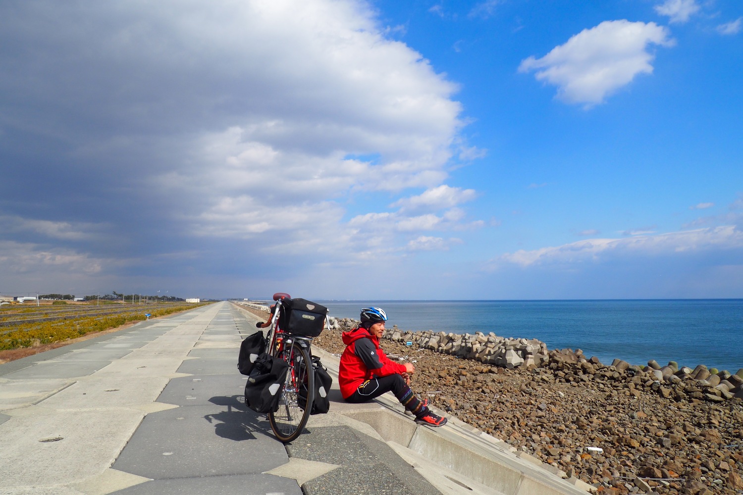 海岸で座るシェルパ斉藤。すぐうしろに自転車