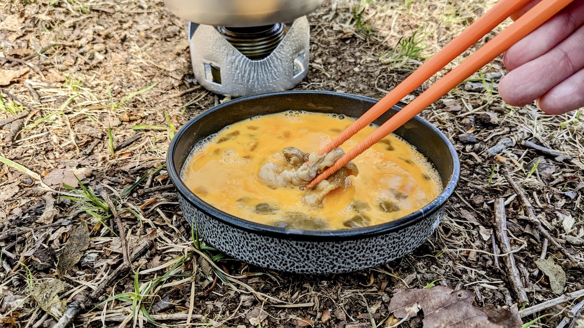 ミニフライパンに入れた生卵に、肉をつけている。