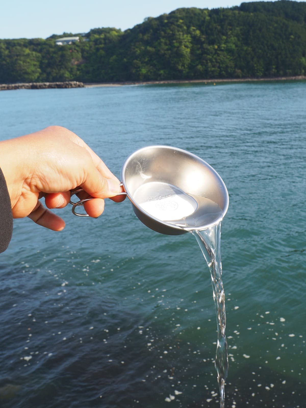 シェラカップの水を海に注ぐ