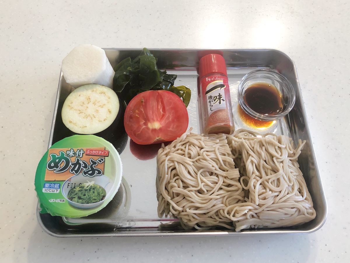 バットの上の流水麺そば、山芋、なす、トマト、一味、めんつゆ、めかぶ。