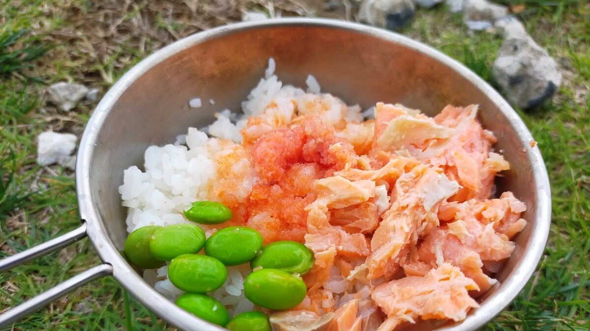 シェラカップの中にお米が入っており、その上に枝豆、鮭、明太子が乗っている。