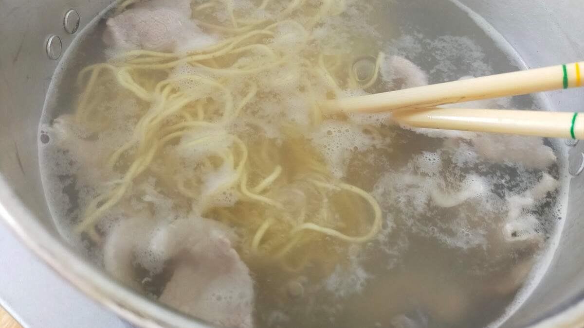 豚肉と袋麺がお湯の中で茹でられている。