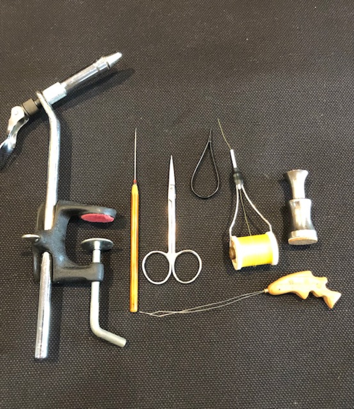 フライタイイングの道具（１セット6,000円〜）。 左からバイス（万力）、ニードル、ハサミ、タイイングスレッドをセットしたボビンホルダー、スッタカー（毛先を揃える道具）、手前にあるのはスレッダー（糸通し）。