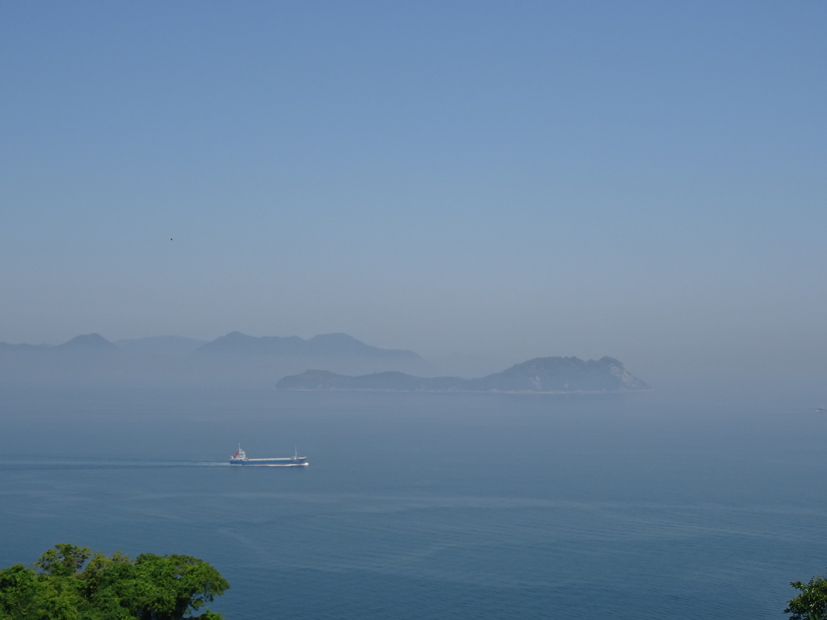 広く穏やかな青い瀬戸内海の海。遠くに島が２つ。手前を、一隻のタンカーが走っている