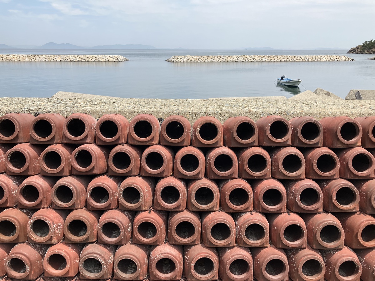 海を背景に、手前に赤茶色の蛸壺が口をコチラ側に向けてキレイに並べられている。