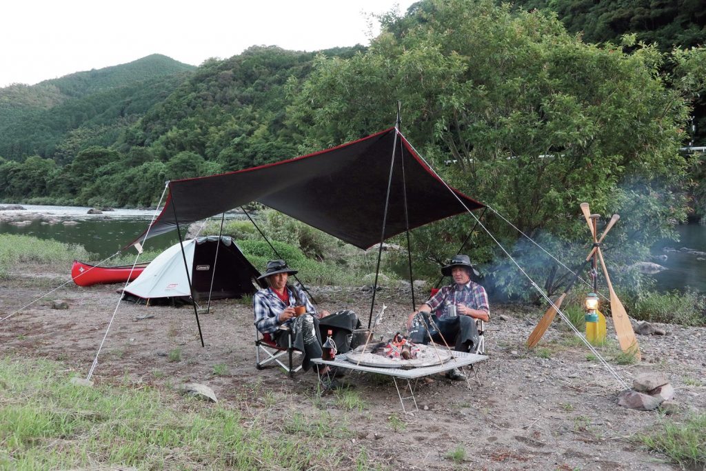 黒いタープの下で魚を焼く男性2人