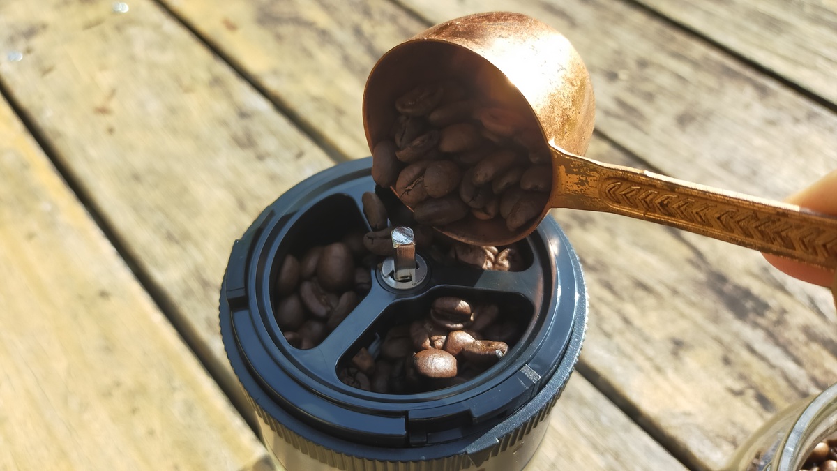 コーヒー豆をコーヒーミルの上部に入れている様子。