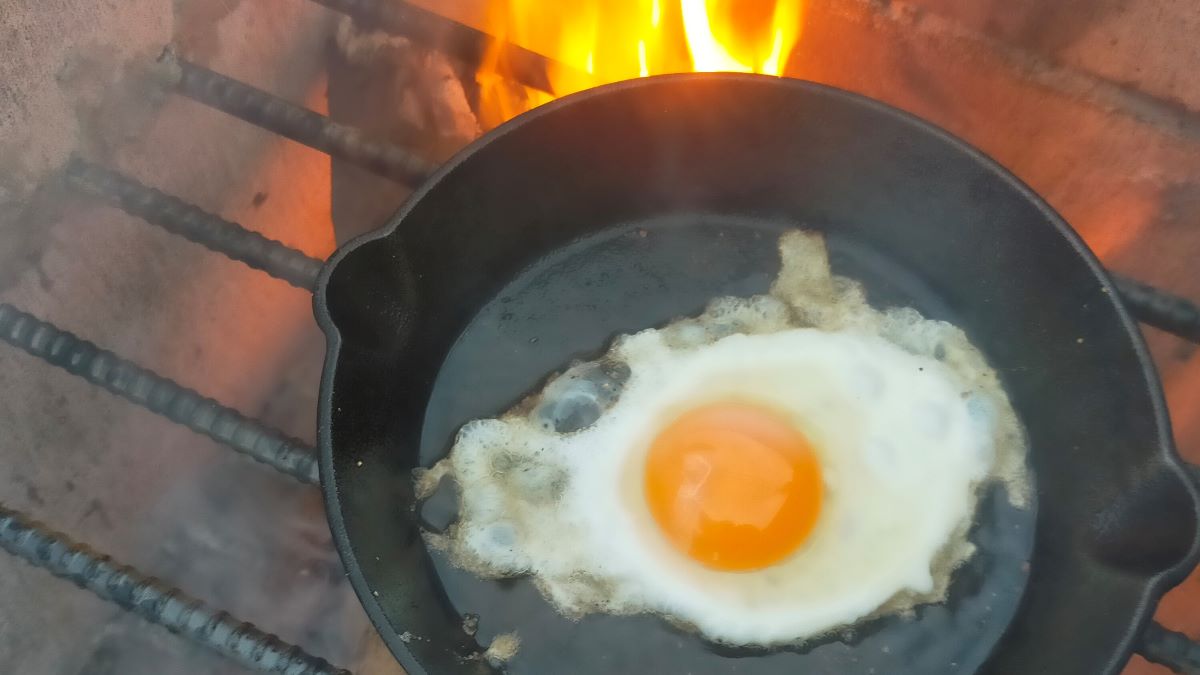 焚き火を使ってスキレットで目玉焼きを作っている様子。