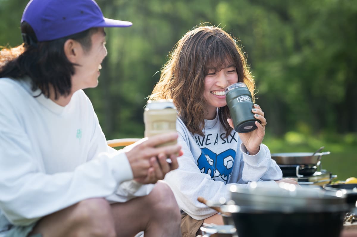 キャンプで飲み物を飲みながら談笑する男女