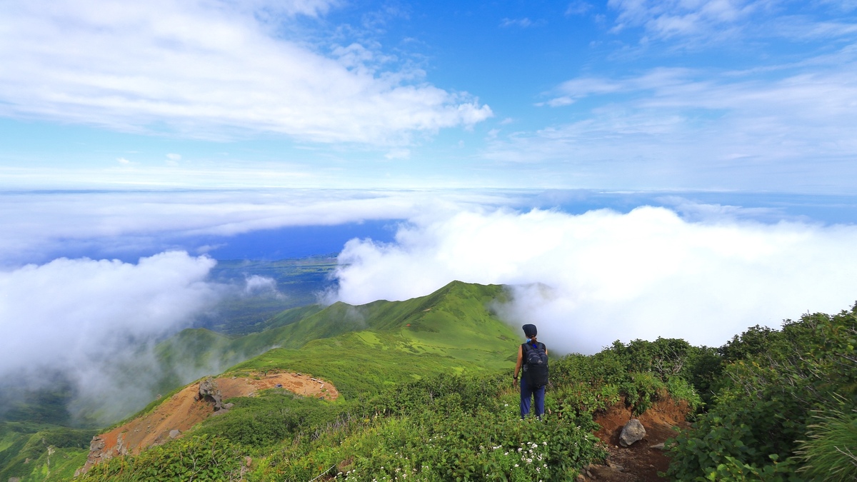 雲海の登山道の上に女性が立っている。