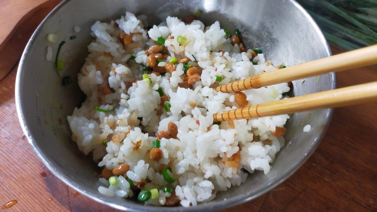 納豆などの具材とご飯を箸で混ぜている。