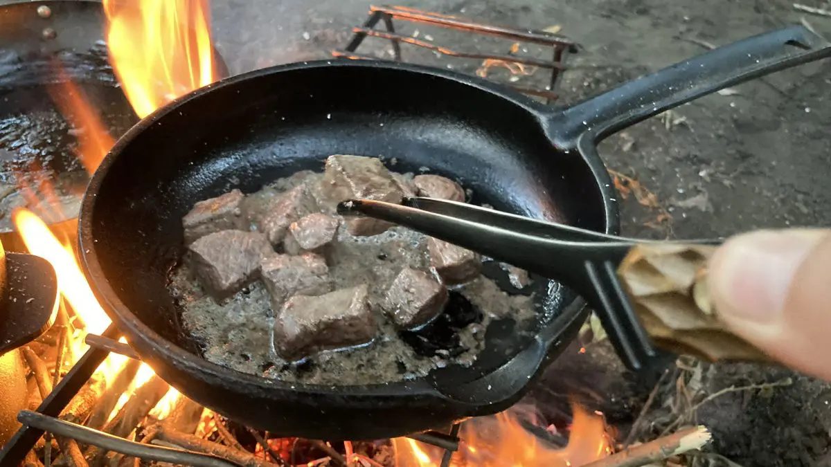 肉をトングで炒める様子