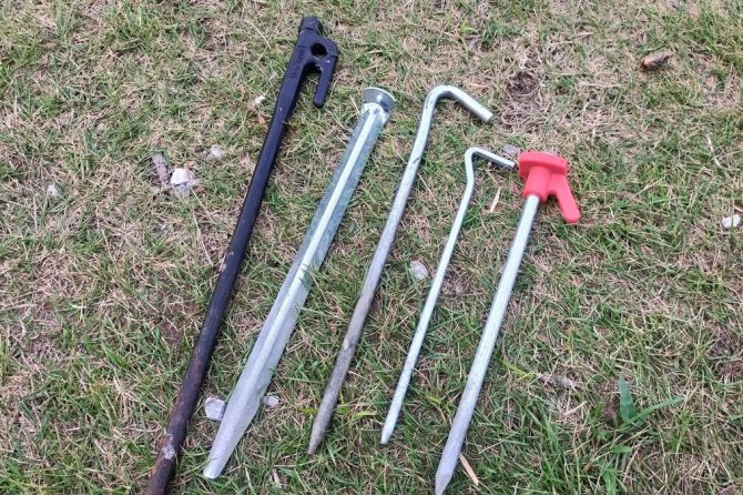 さまざまなタイプのテントペグが地面に並んでいる様子。