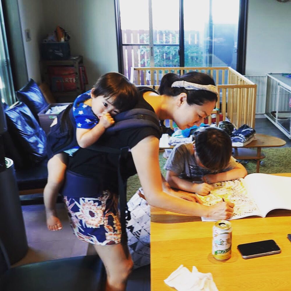 生まれたばかりの次男を背負いながら、ぬりえを手伝う筆者