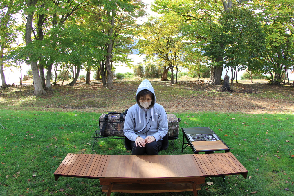 キャンプテーブルの前に座り、正面を向いている「Helinox タクティカル スウィベル チェア」の使用シーン。