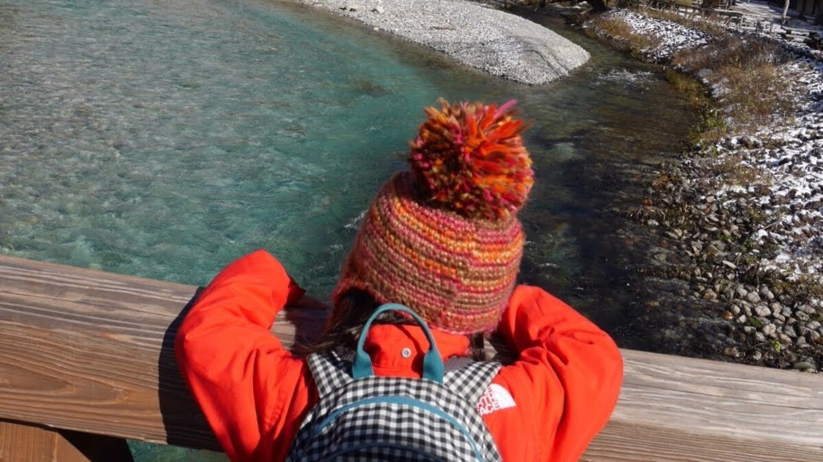 冬服を着こんだ子どもが川を眺めている。