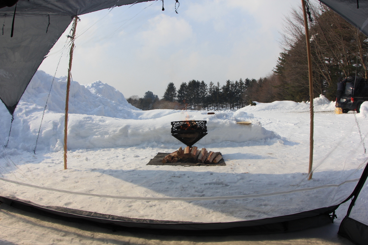 TPUウィンドウ越しに焚き火台を眺める構図。雪景色と炎が透明パネル越しに見えている様子。