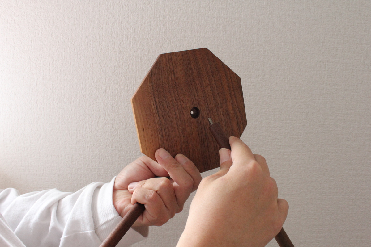 八角形の木製棚板にポールを差し込み、固定しようとしている手元の写真。